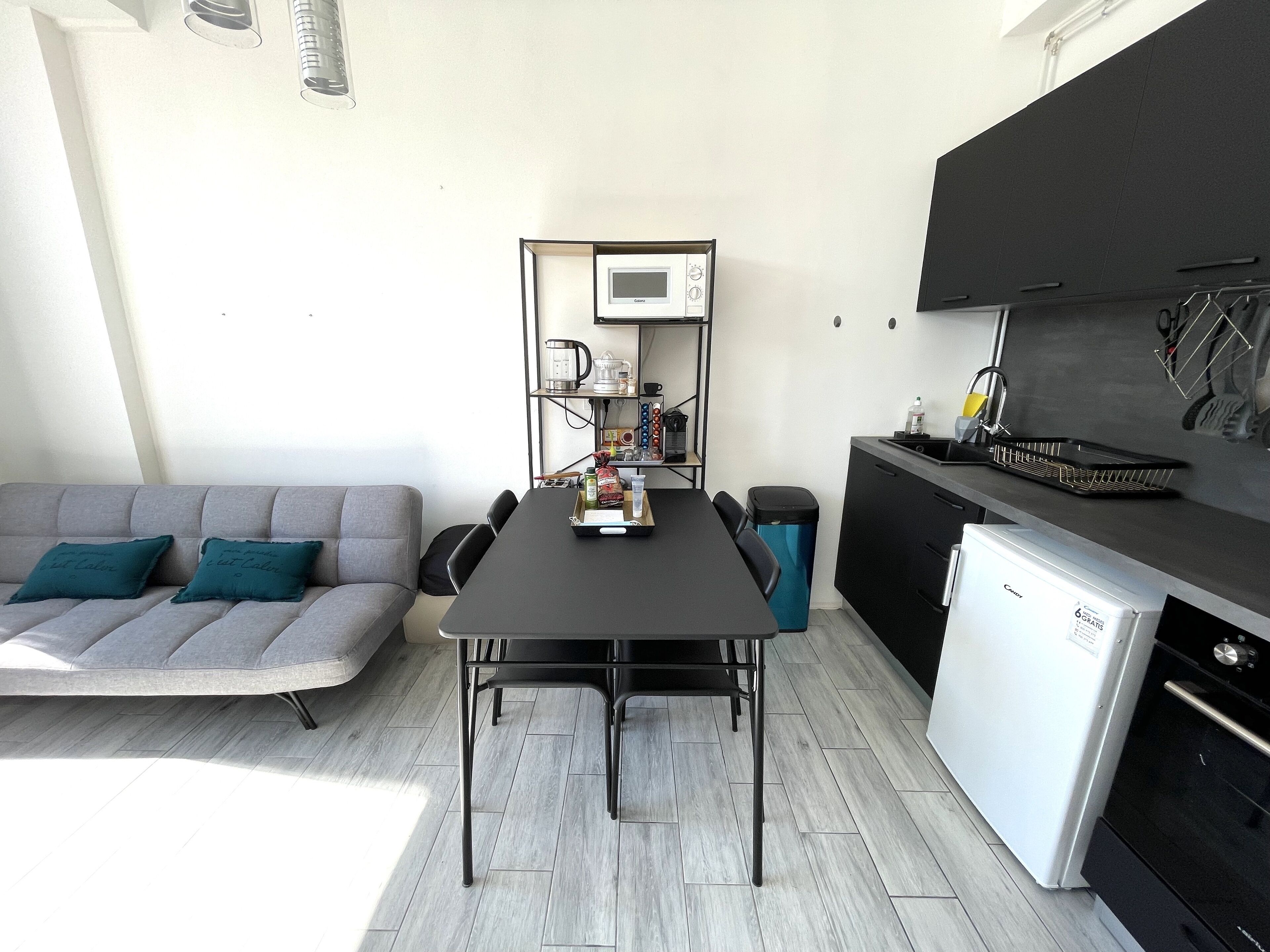 A compact living space with a sofa, dining table, kitchenette, and a small refrigerator.