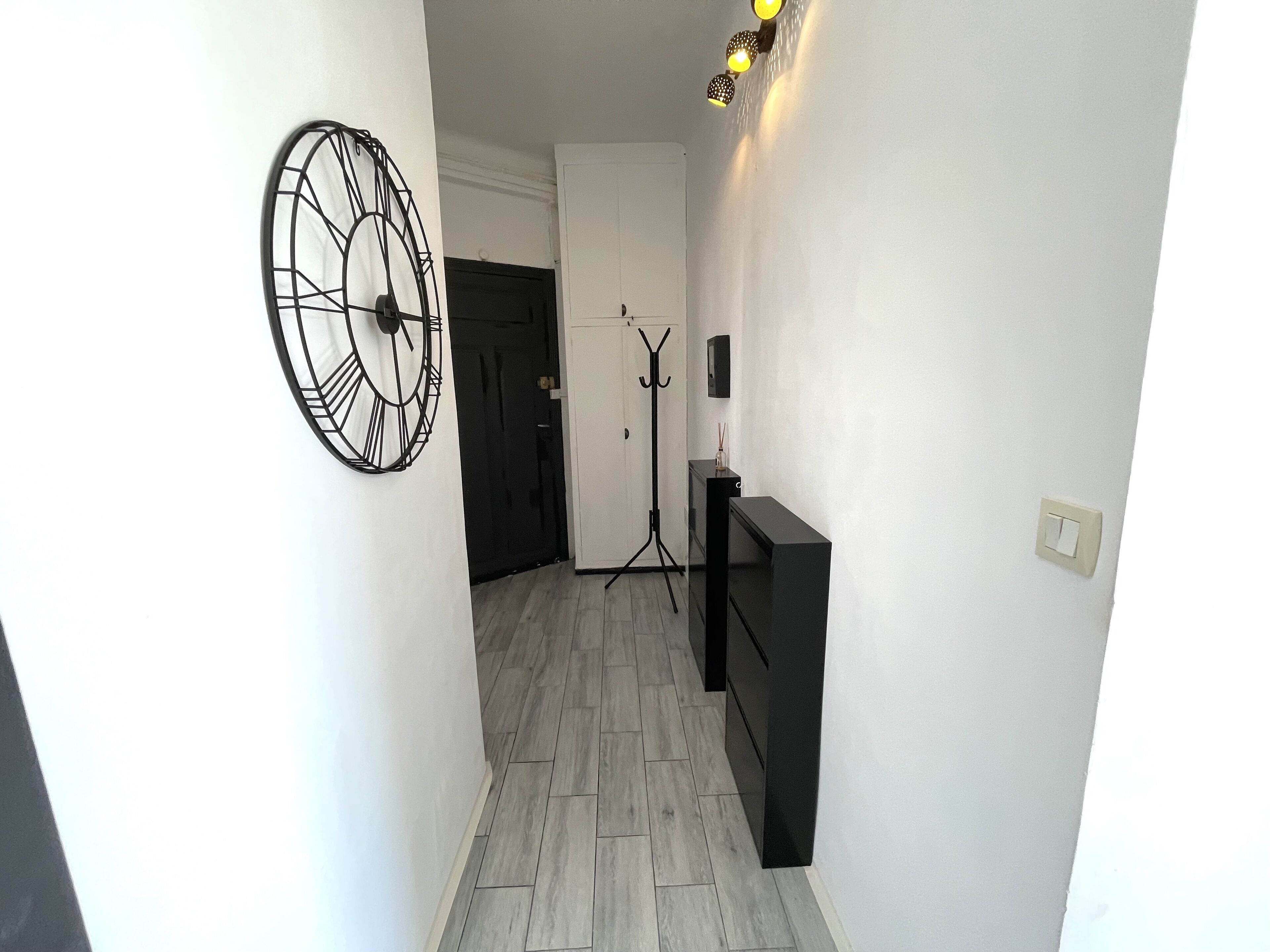 Un couloir avec une horloge, un porte-manteau et un lampadaire.