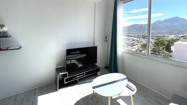 A modern living room with a large window, a flat-screen TV, a small table, and a shelf with a globe and books. - Calvi T2 air-conditioned, wifi, city center, near the beach, shops, cab & train station. (Calvi)