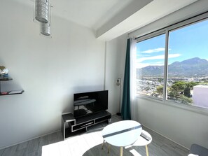 A modern living room with a large window, a flat-screen TV, a small table, and a shelf with a globe and books. - Calvi T2 air-conditioned, wifi, city center, near the beach, shops, cab & train station. (Calvi)