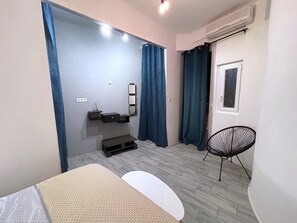A modern bedroom with a bed, a small table, a chair, a built-in shelf, and a window with curtains. - Calvi T2 air-conditioned, wifi, city center, near the beach, shops, cab & train station. (Calvi)