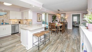 A modern kitchen with white cabinets, a marble countertop, and wooden stools. - Oceanviews-Steps 2 Beach-Stunning-MultiBalconies-Gated Community-Pool/Hottub (Myrtle Beach)
