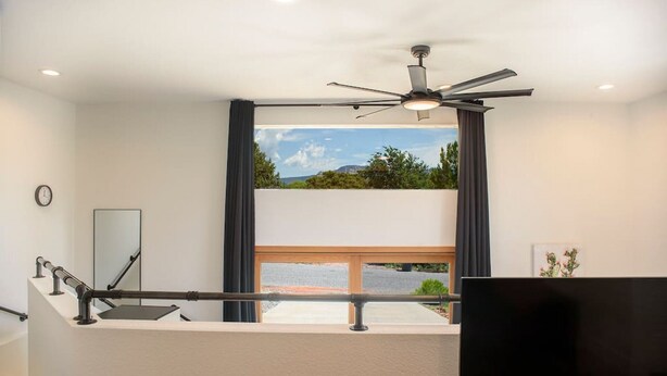 Une chambre moderne dotée d’un balcon, d’un ventilateur de plafond, d’une grande fenêtre avec des rideaux, d’un téléviseur à écran plat et d’une horloge murale.