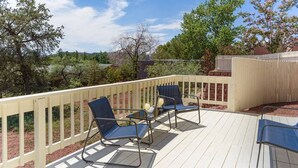 Une terrasse avec deux chaises bleues et une petite table, entourée d’une balustrade blanche.