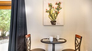 Une pièce avec deux chaises, une petite table sur laquelle sont posées deux tasses blanches, et un tableau représentant un cactus accroché au mur.