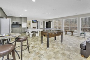 Una cocina amplia con mesa de fútbol, un comedor con mesa y sillas, y ventanas grandes que ofrecen vistas al exterior.
