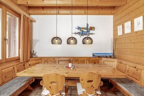 A wooden dining room with a large table, benches, and pendant lights.