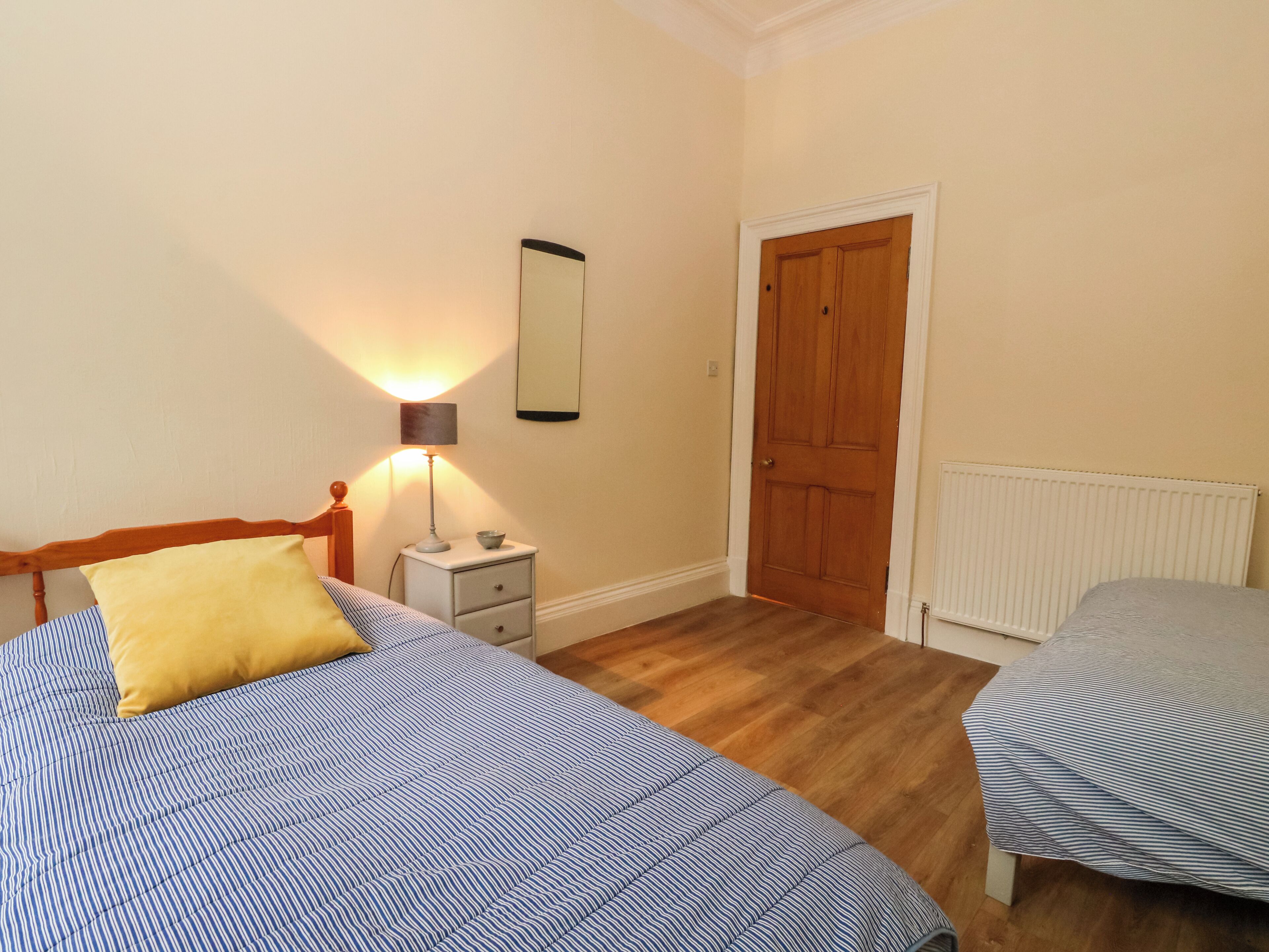 Une chambre avec deux lits, une table de chevet, une lampe, un miroir, une porte et un radiateur.
