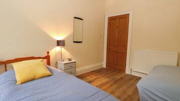 Une chambre avec deux lits, une table de chevet, une lampe, un miroir, une porte et un radiateur.