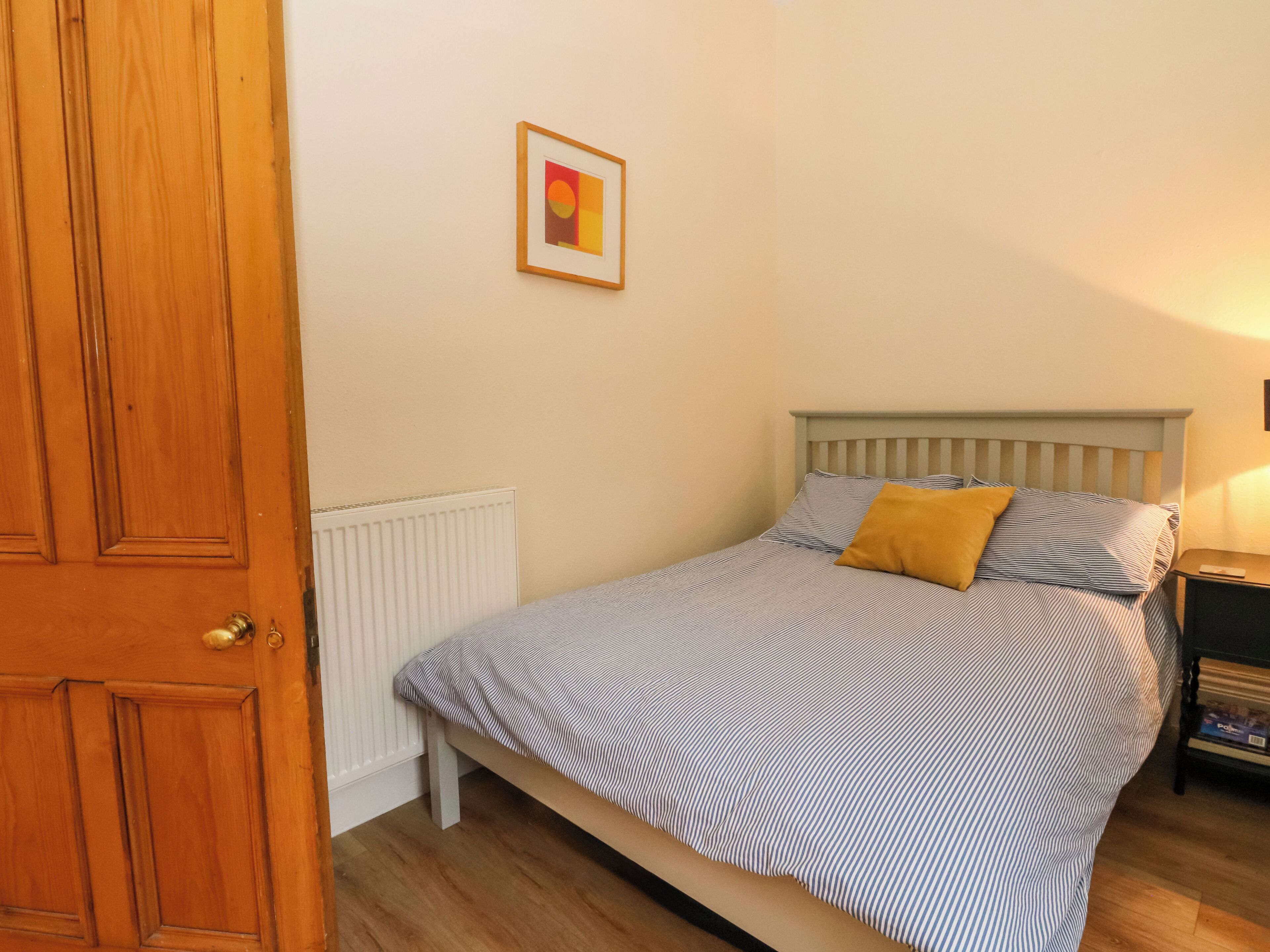 A bedroom with a bed, a wooden door, a radiator, and a framed picture on the wall.