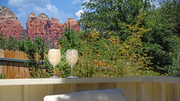 A balcony with two glasses of a light-colored beverage, a wooden fence, and a view of red rock formations. - Modern Zen Luxury · With Views · Centrally Located (Sedona)