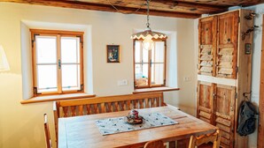 A cozy dining area with a wooden table and bench, two windows with curtains, and a wooden wardrobe with a coat hanging on it. - Vacation home Fichte (4822 Bad Goisern am Hallstättersee)