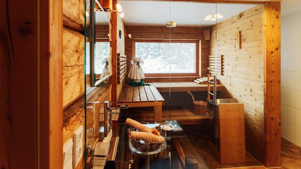 A wooden cabin interior with a wooden dining table, a bench, and a window with a view of trees. - Vacation home Fichte (4822 Bad Goisern am Hallstättersee)