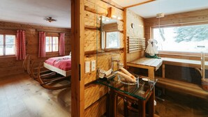 A wooden cabin interior with a bed, a glass table with food, and a window with a view of trees. - Vacation home Fichte (4822 Bad Goisern am Hallstättersee)