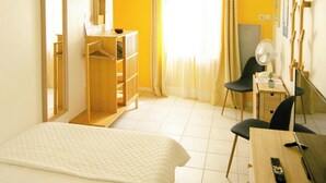 A hotel room with a bed, a desk with a chair, a mirror, a wardrobe, and a window with curtains.