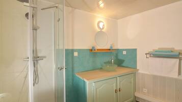 Une salle de bain avec une douche, un lavabo avec un miroir au-dessus et un porte-serviettes.