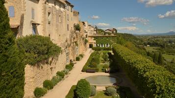 Un bâtiment historique en pierre, avec un jardin et un sentier menant à un étang.