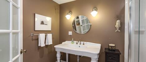 A bathroom with a white sink, two wall-mounted lights, a round mirror, a framed picture, and a decorative fish on the wall.