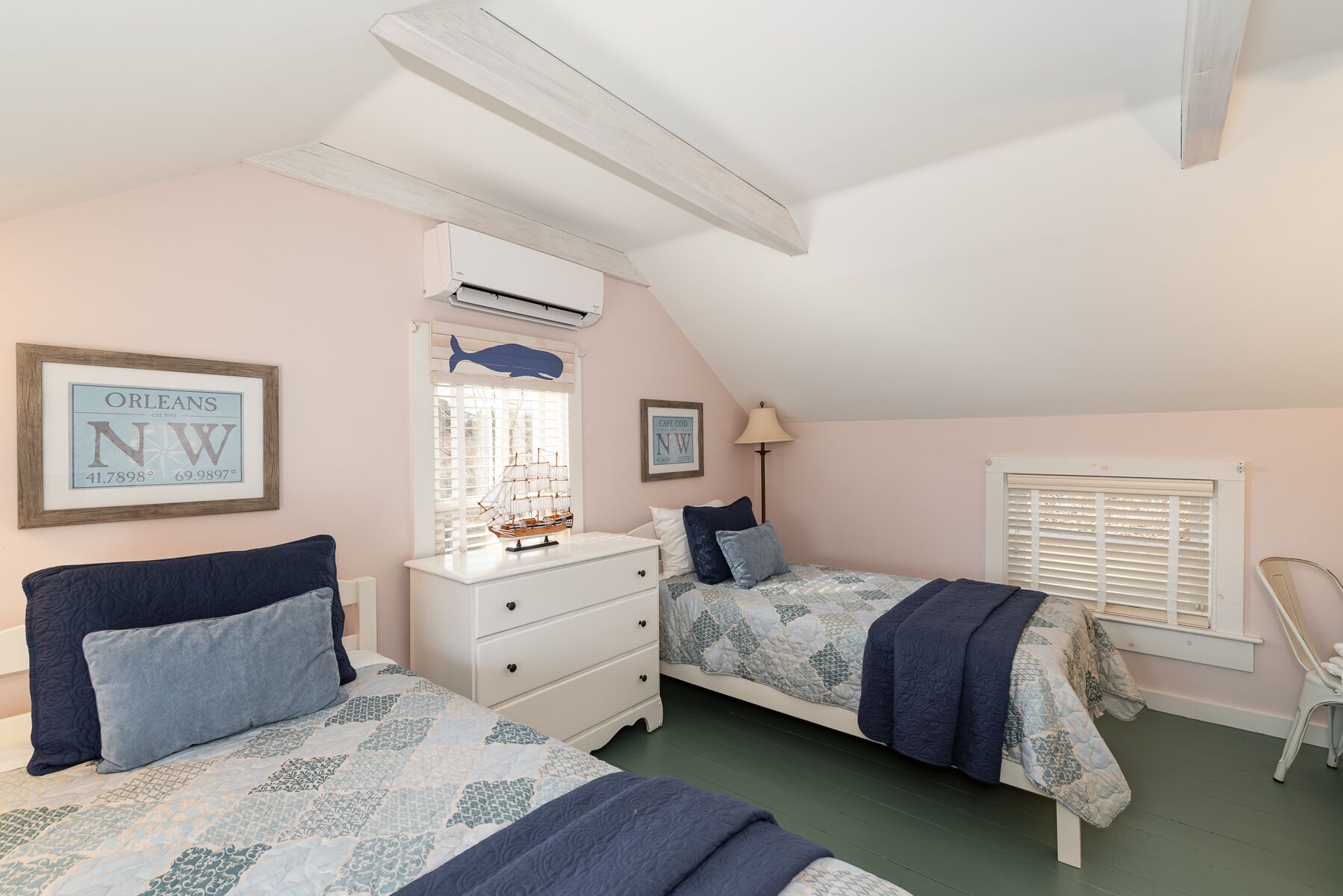 A bedroom with two beds, a dresser, a lamp, and a window with blinds.