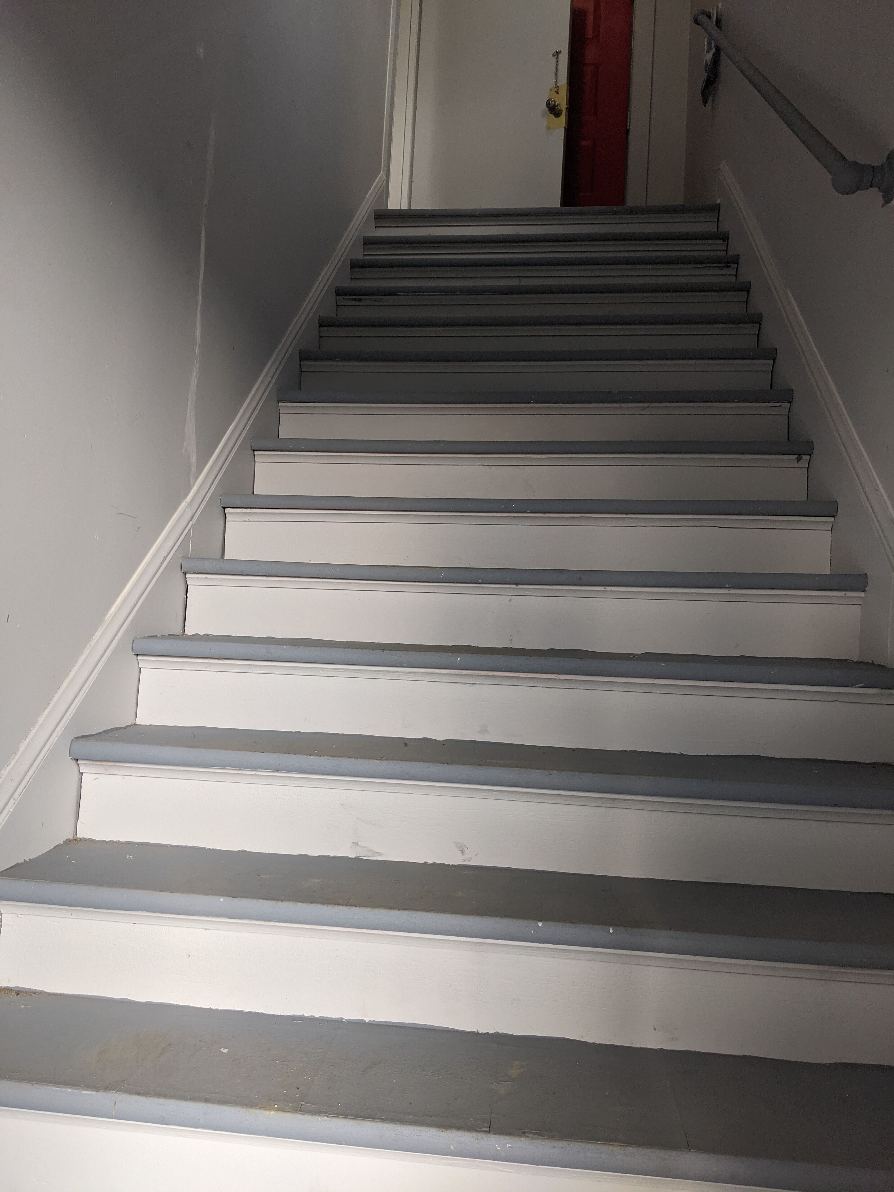 Una scala con gradini bianchi e una porta rossa in cima.