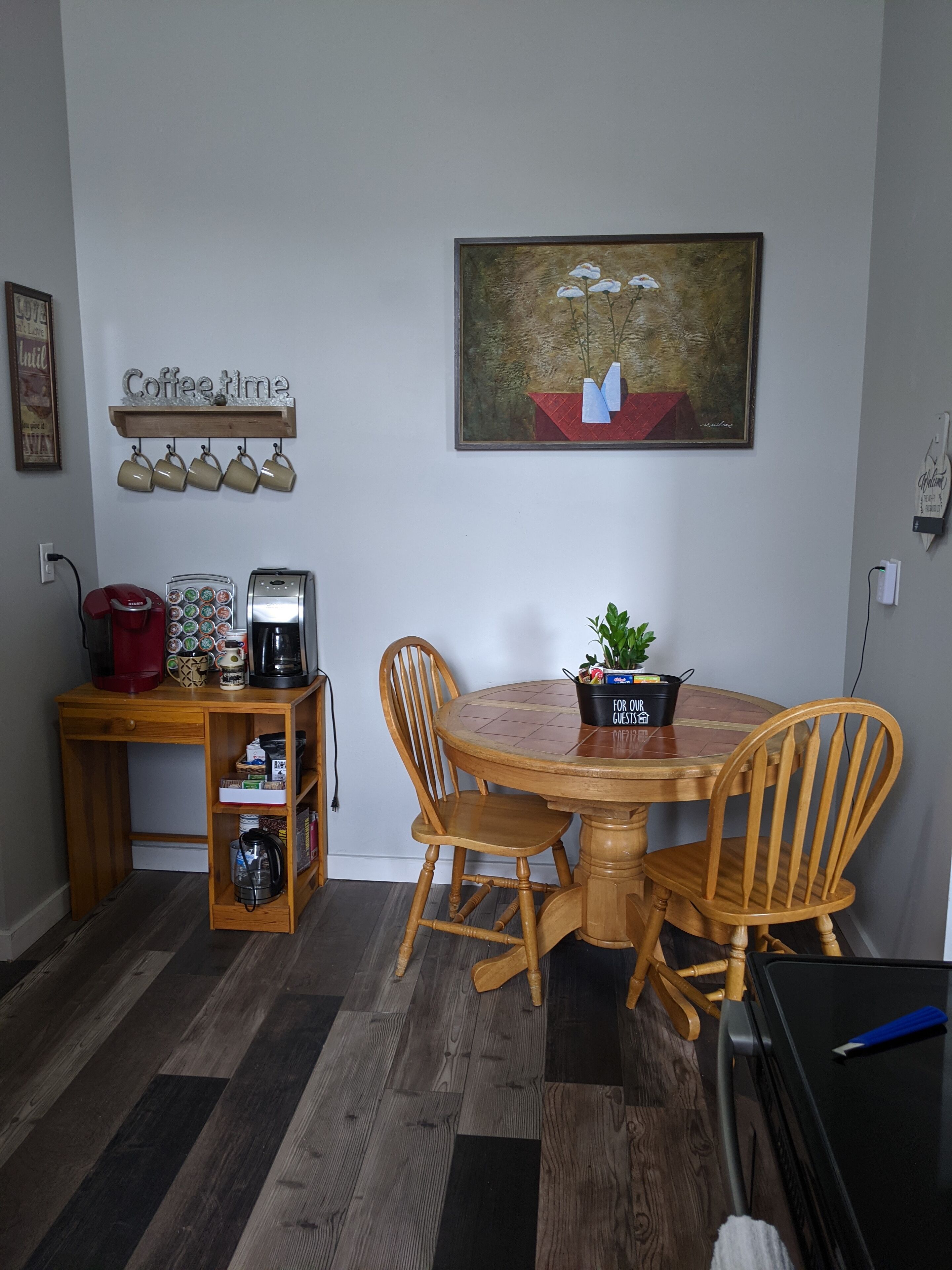 Ein Essbereich mit einem Holztisch und Stühlen, einer Kaffeestation mit Tassen und einer Kaffeemaschine sowie einem Gemälde an der Wand.