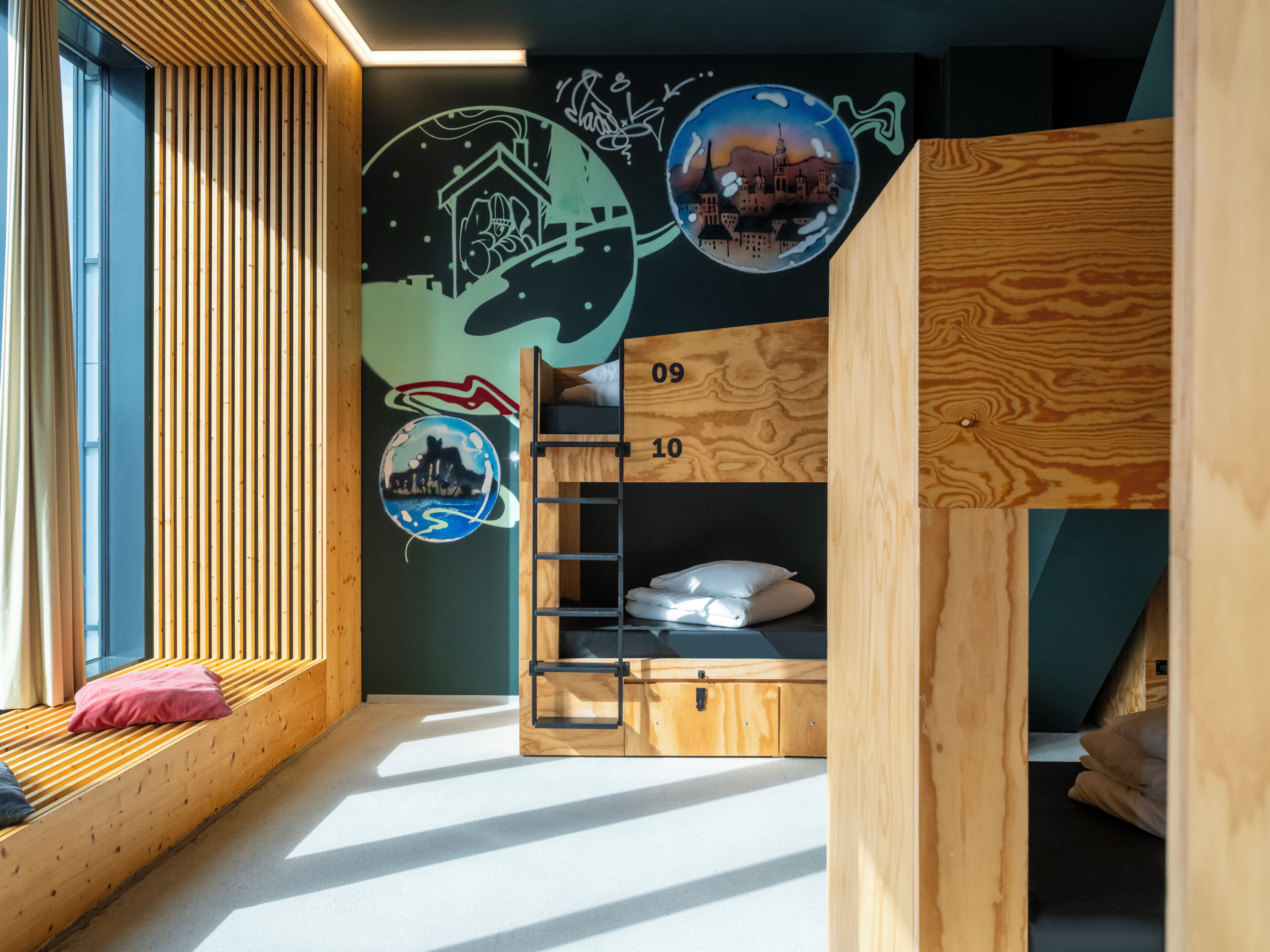 A child's bunk bed with a ladder, a window with curtains, and a wall with two circular murals.