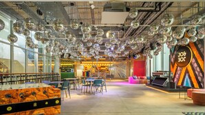 A modern lounge area with multiple seating options, a bar, and disco balls hanging from the ceiling. - JO&JOE Vienna - Hostel (Vienna)