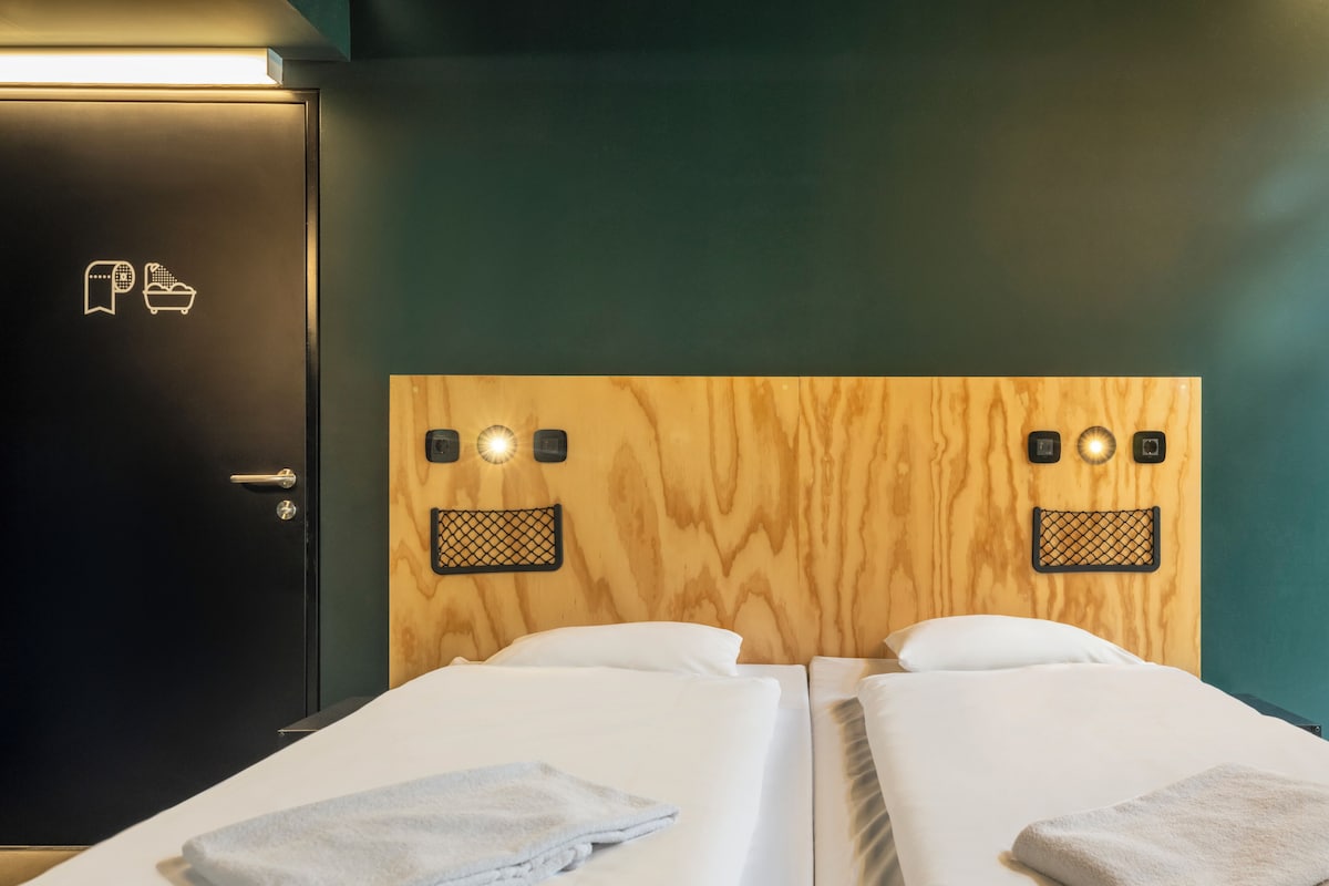 Une chambre d’hôtel avec deux lits simples, une tête de lit en bois, une porte noire et une serviette sur chaque lit.