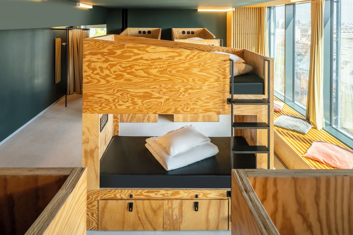 Une chambre moderne et compacte, dotée de lits superposés et d’une fenêtre donnant sur un paysage urbain.