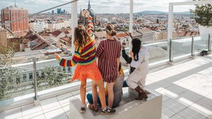 A group of people on a high balcony overlooking a cityscape with buildings and a church spire. - JO&JOE Vienna - Hostel (Vienna)