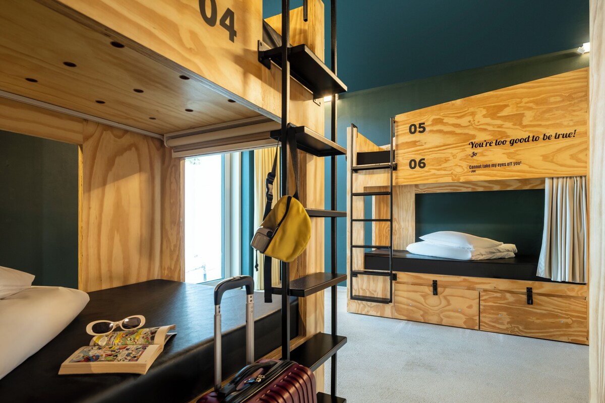 Une chambre avec un lit superposé, une valise, une paire de lunettes de soleil et un livre posés sur le lit.