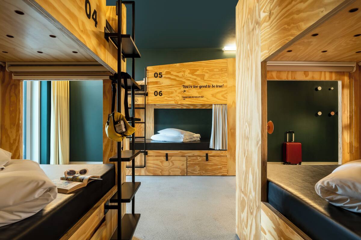 Une pièce avec des lits superposés, un mur en bois orné de chiffres, une valise et une étagère fixée au mur.