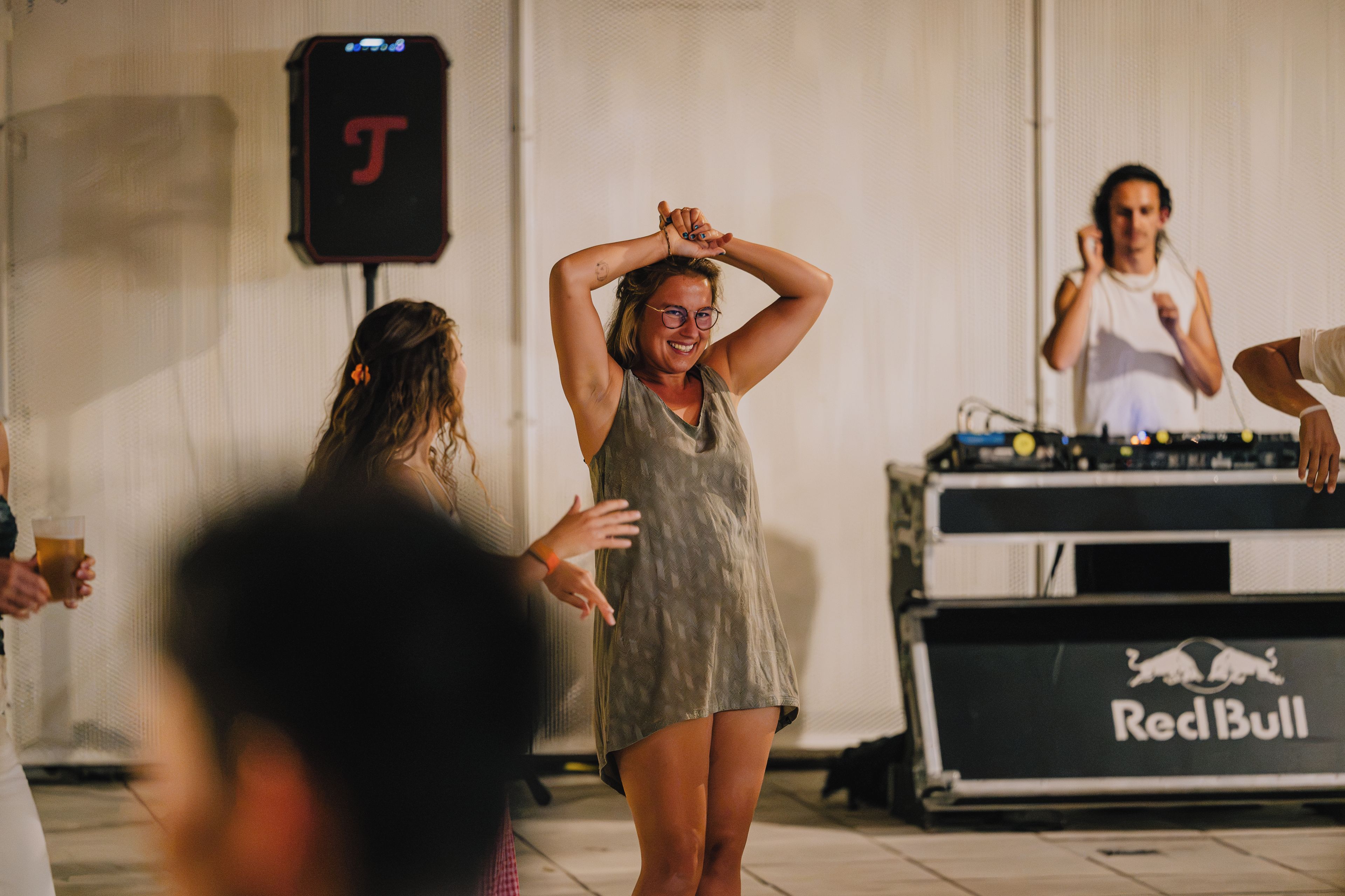 A person in a sleeveless dress with a DJ booth in the background.