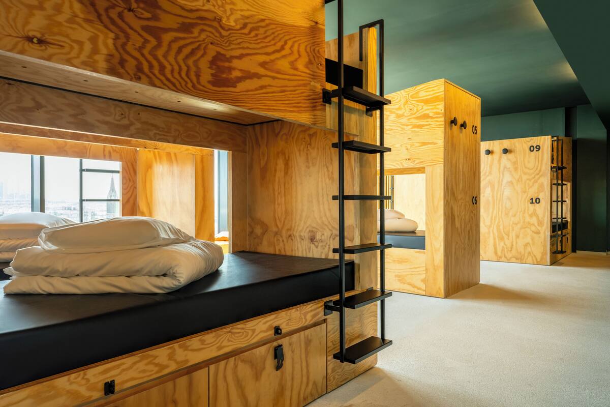 Une pièce en bois avec un lit superposé, une échelle et une fenêtre donnant sur la ville.