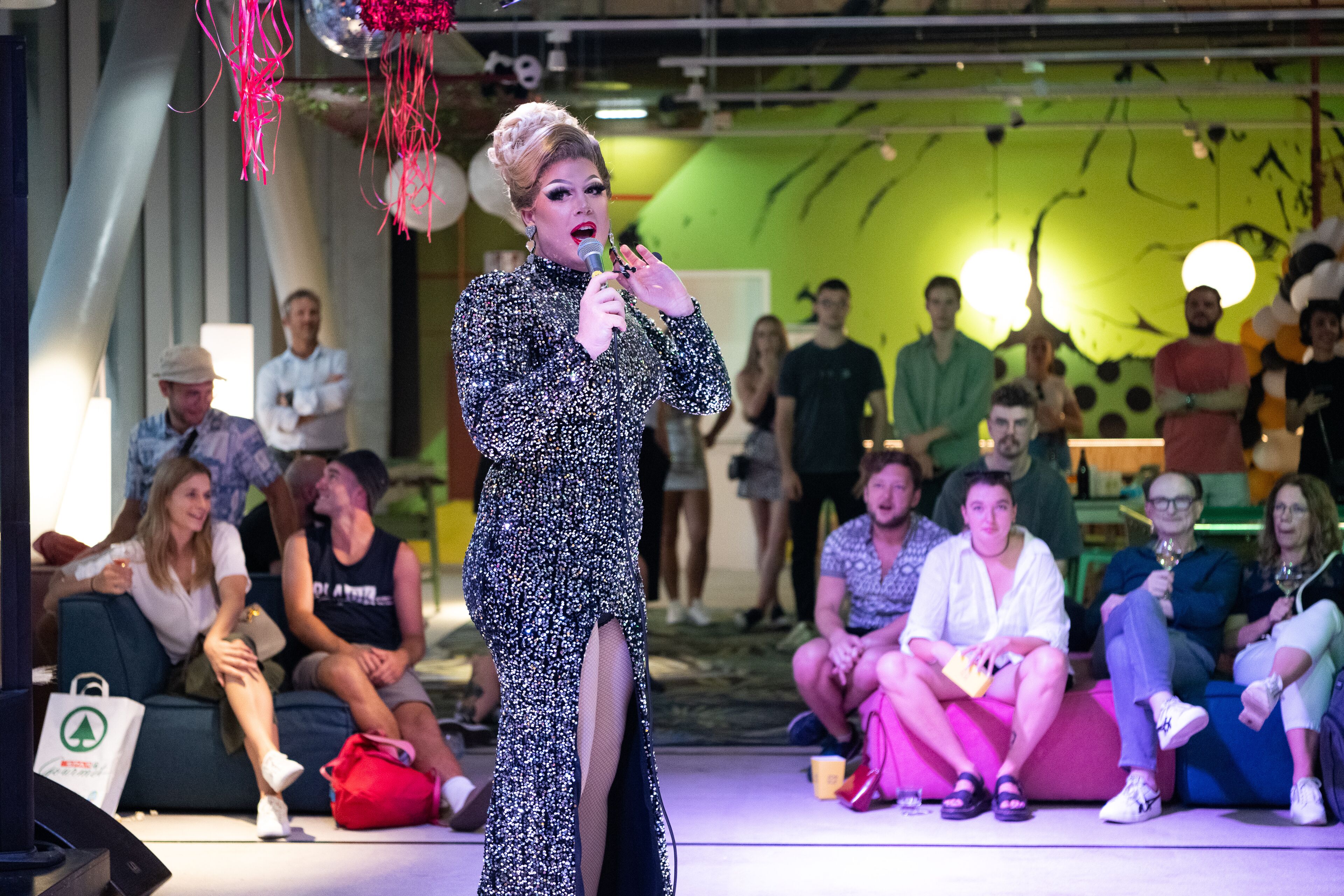 Uma pessoa se apresentando no palco, com uma plateja sentada ao fundo.