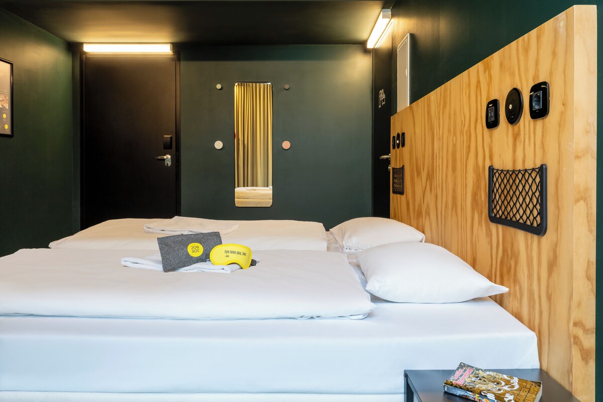 Une chambre d’hôtel avec un lit, une tête de lit en bois, un miroir et une petite table sur laquelle se trouve un magazine.