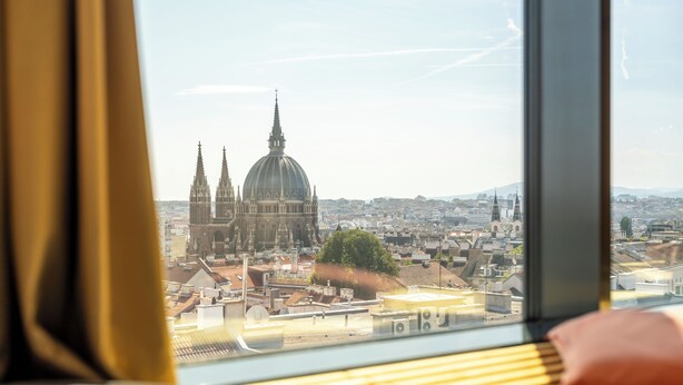 A window view of a cityscape with a prominent cathedral and surrounding buildings. - JO&JOE Vienna - Hostel (Vienna)