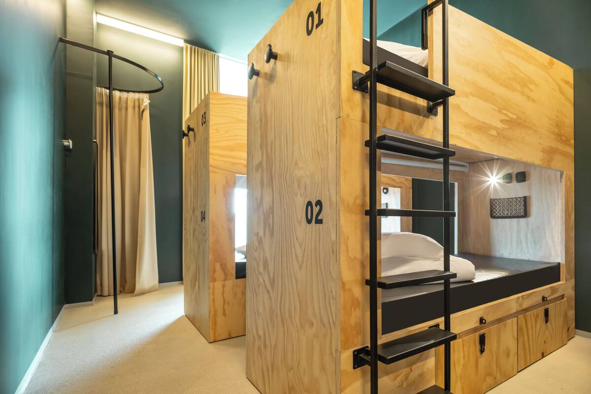 Une chambre avec un lit superposé en bois, une échelle, des portes numérotées et une petite étagère.
