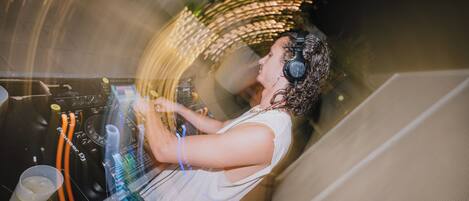 A person DJing with a mixer and headphones, surrounded by equipment and cables.
