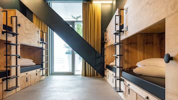 Een moderne hotelkamer met stapelbedden, houten wanden en een trap naar een balkon.