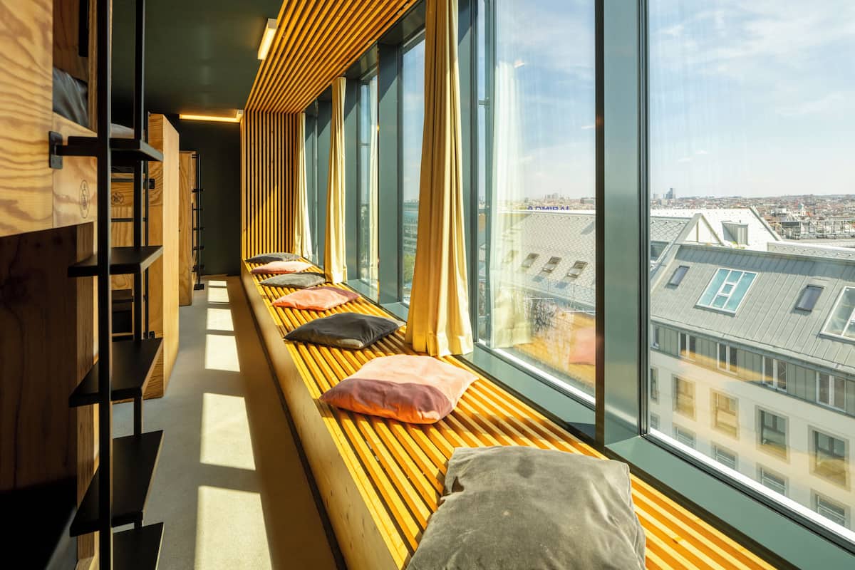 Une rangée de bancs en bois avec des coussins, une bibliothèque en bois et de grandes fenêtres donnant sur la ville.