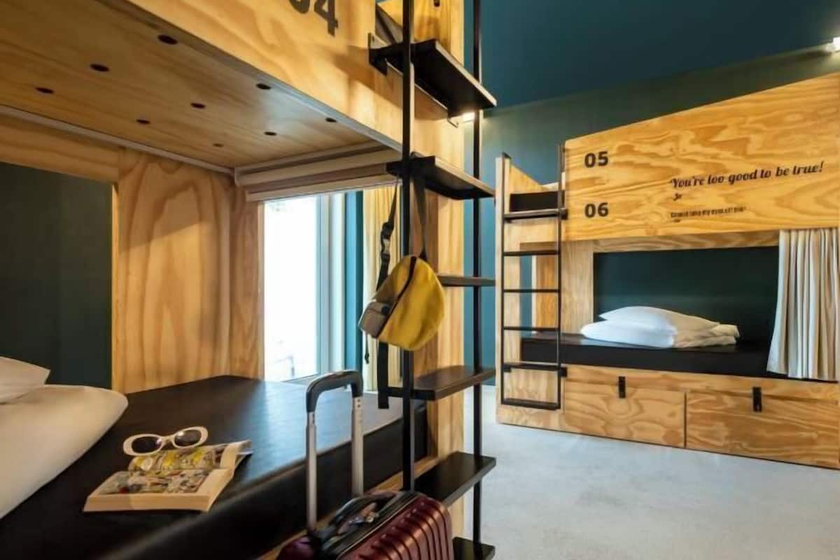 Une chambre avec un lit superposé, des murs en bois, un bureau avec une valise et une fenêtre.