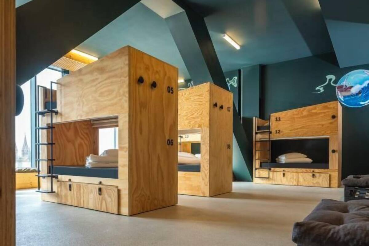 Une chambre avec des lits superposés numérotés de 05 à 12, des meubles en bois et une échelle.