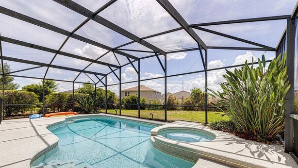 A swimming pool with a glass enclosure, surrounded by a concrete deck and plants.