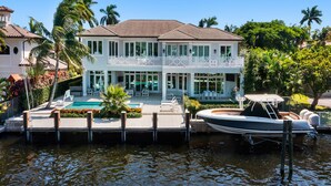 A waterfront property with a pool, boat dock, and lush greenery.