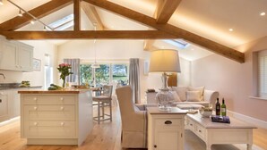 A spacious loft with a high ceiling, wooden beams, a kitchen with white cabinets, a dining area with a table and chairs, and a living room with a sofa and a coffee table.