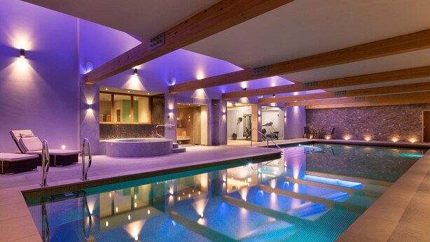 A modern indoor swimming pool with a jacuzzi, lounge chairs, and a stone wall. - Honister Cottage - Luxury Cottages (Kendal)