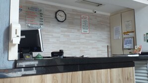 A hotel reception desk with a clock, a Coca-Cola sign, and a sign listing room rates. - Hotel Michel (São Paulo)
