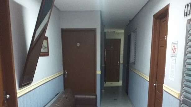 A hallway with a brown sofa, tiled floor, and doors on both sides. - Hotel Michel (São Paulo)