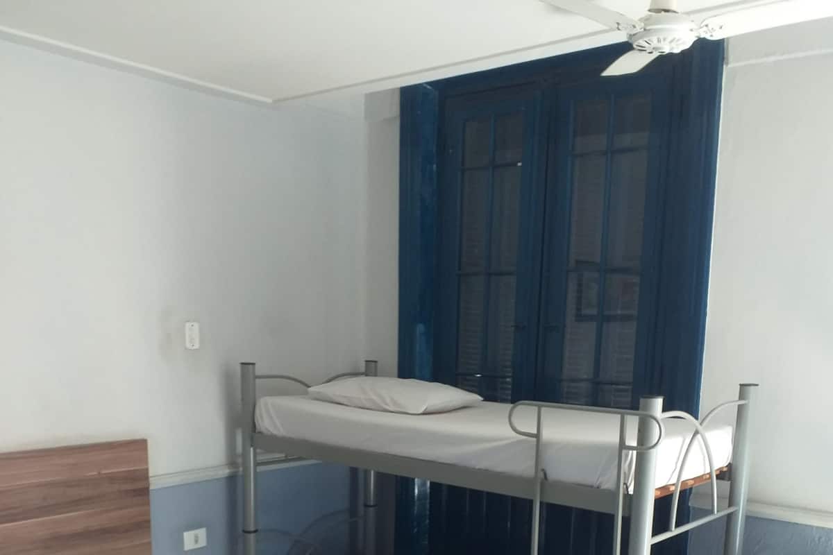 A bunk bed room with a desk and chair, a ceiling fan, and a window with blue curtains.